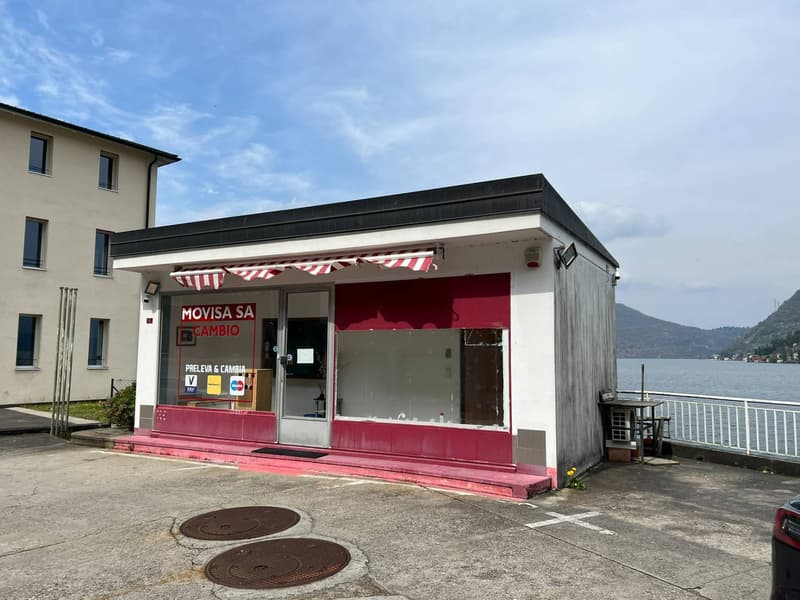 Small office building near water, red trim, windows, outdoor table, parking lot, mountains in the distance