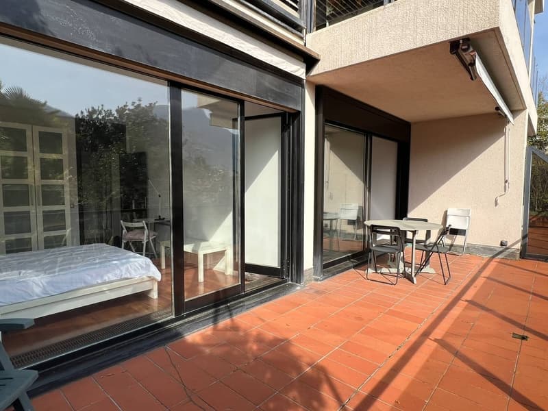 Bedroom with bed, glass doors, balcony with table and chairs, and a view of the outside