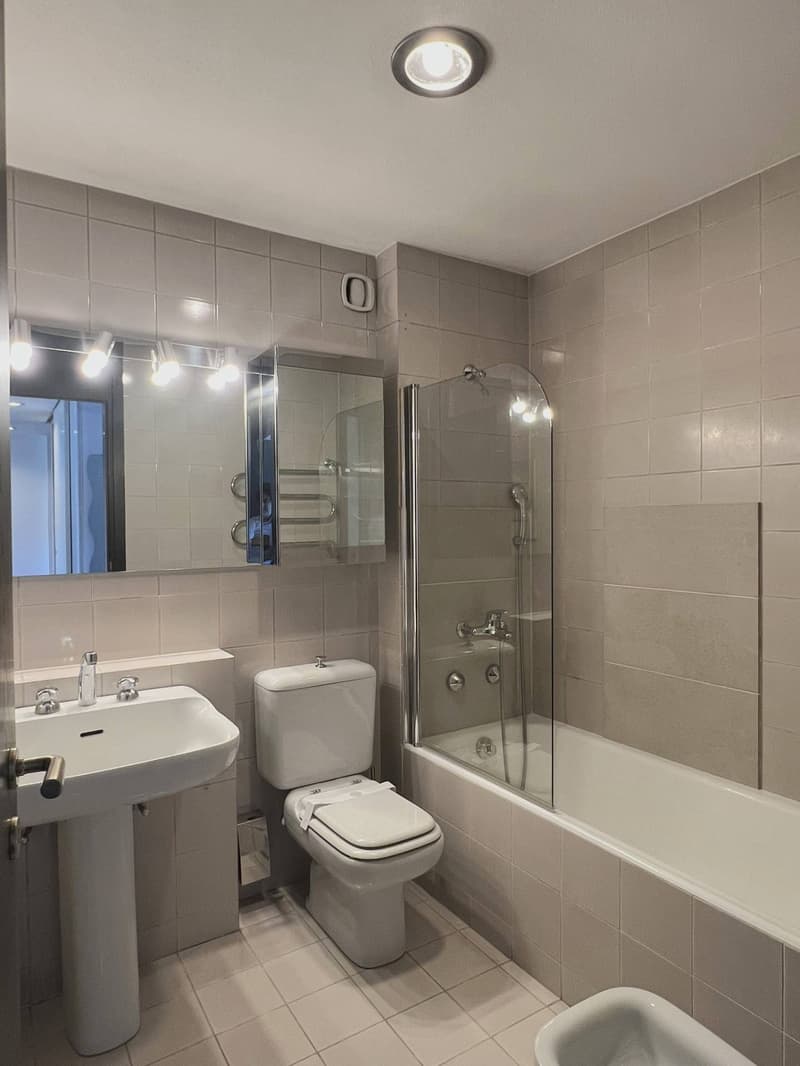 Bathroom with white tiles, white sink, white toilet, glass shower enclosure, bathtub, mirror, and towel rack.