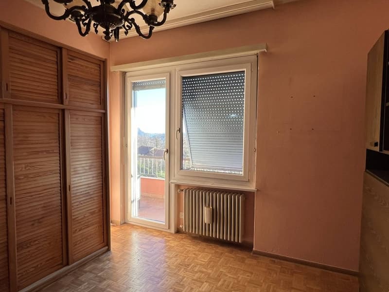 Empty room with wooden floor, pink walls, wooden wardrobe, sliding glass door, balcony, white radiator