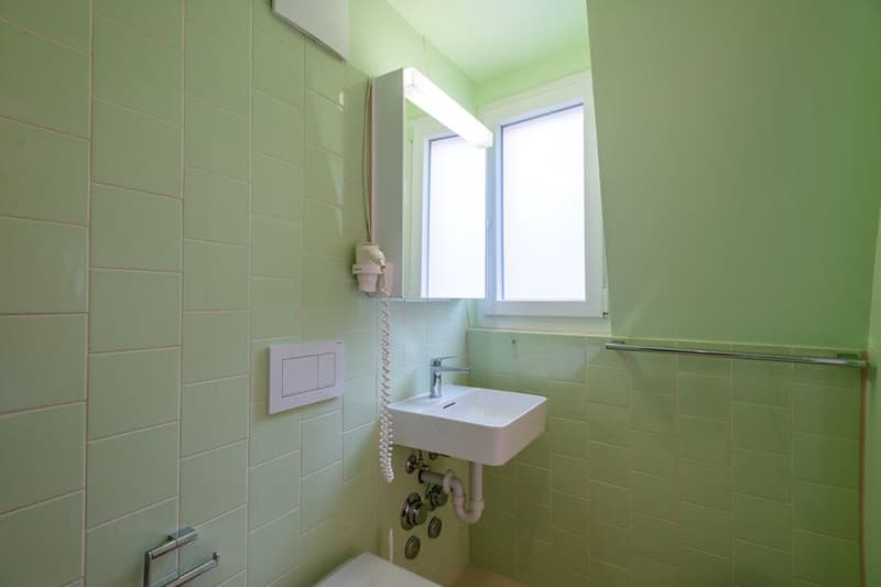 Small bathroom with green tile walls, a white sink, and a window