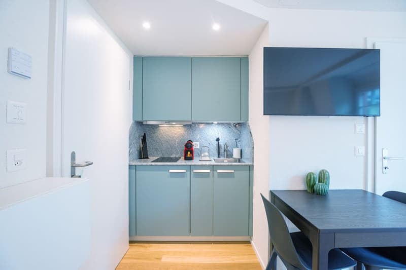 Modern kitchen with light blue cabinets, stainless steel appliances, and a large TV mounted on the wall. The kitchen also features a dishwasher.