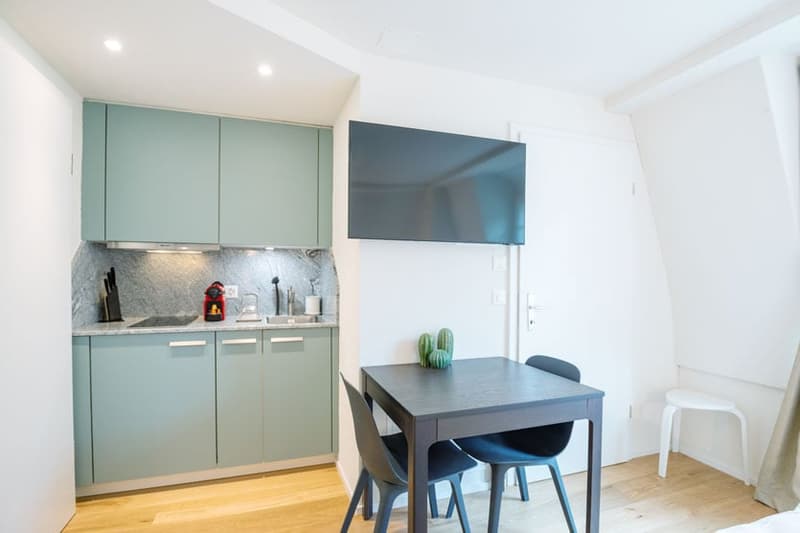 Modern kitchen with mint green cabinets, gray backsplash, built-in dishwasher, and a dining table with dark chairs