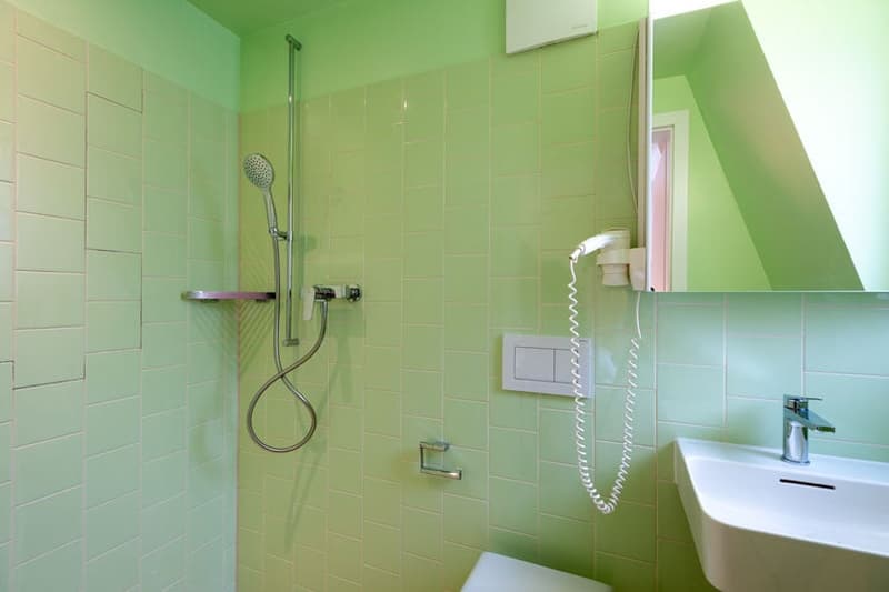 Green tiled bathroom with shower, sink, and towel rack