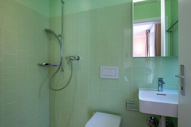Green tiled walls, shower with glass enclosure, sink, toilet