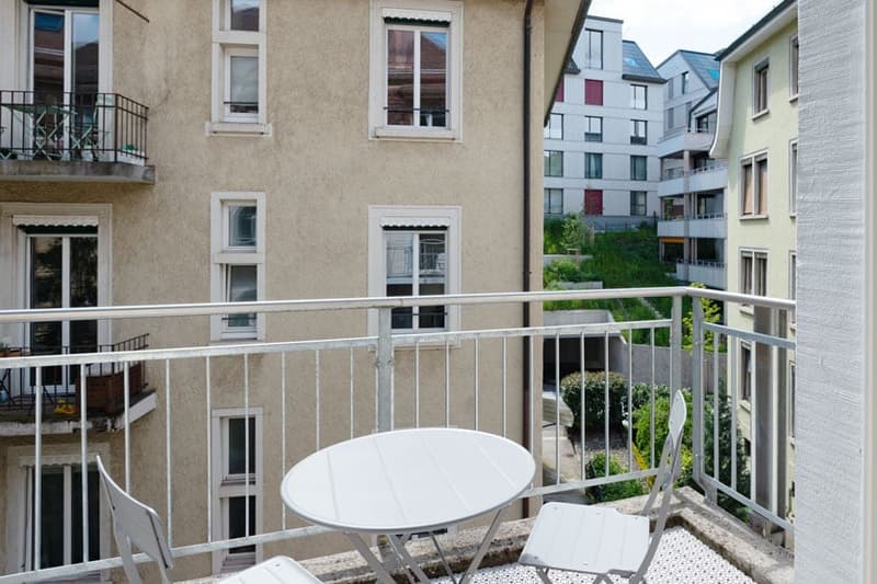 Balcony with a small round table and chairs, overlooking a courtyard with other apartment buildings