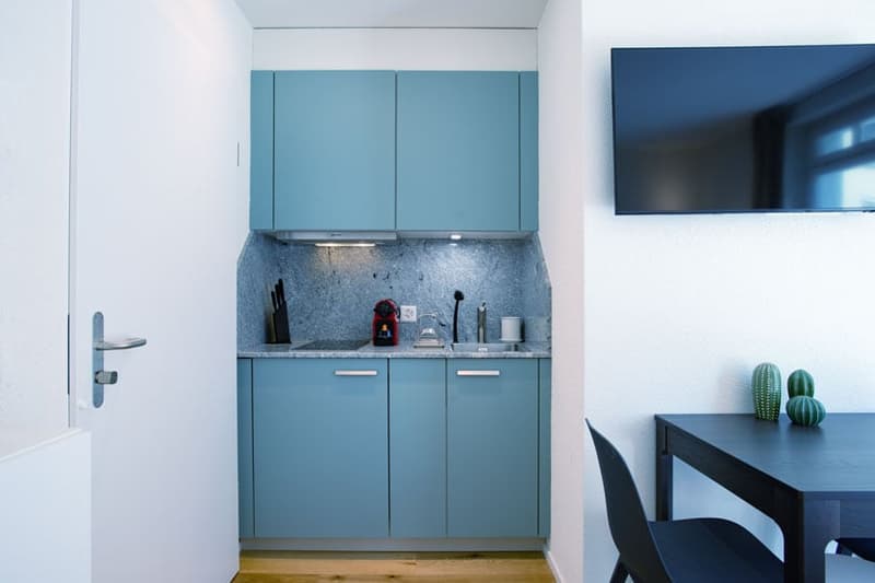 Compact kitchen with blue cabinets, gray countertop, and a dishwasher