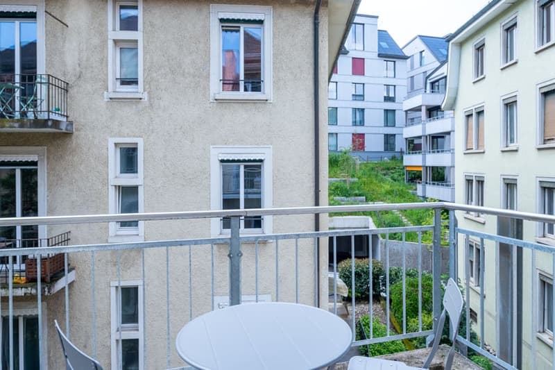 Apartment building with balconies, windows, and greenery visible in the courtyard