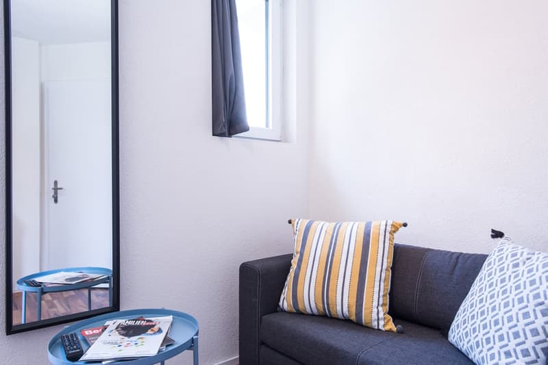 Dark gray sofa, striped throw pillow, side table with magazines, large window with curtains