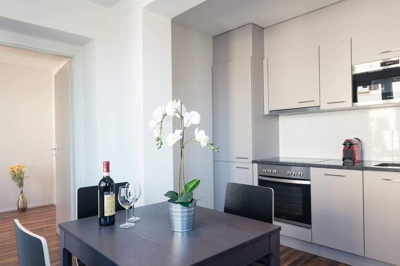 Modern kitchen with white cabinets, black countertop, stove, and dining table with wine glasses and a potted plant