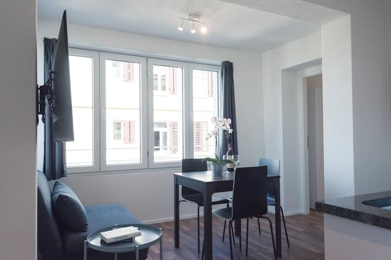 Bright and modern living room with large windows, black dining table and chairs, and an orchid plant on the table