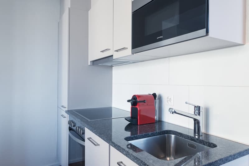Modern kitchen with white cabinets, black granite countertop, built-in microwave, and a red Nespresso coffee machine on the counter.