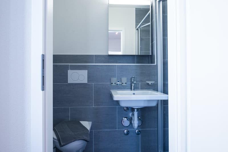 Modern bathroom with gray tile walls, a white sink, and a washing machine