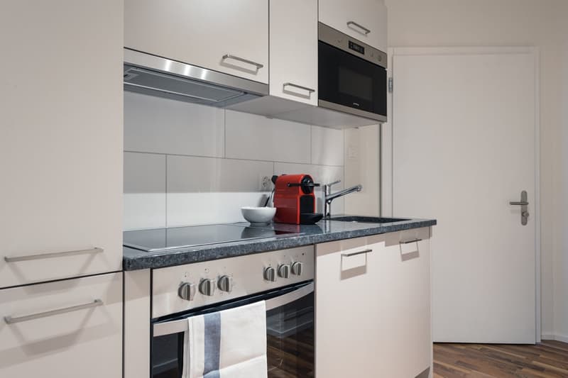 Modern kitchen with white cabinets, stainless steel appliances including a microwave and oven, granite countertop, and a red coffee machine on the counter.