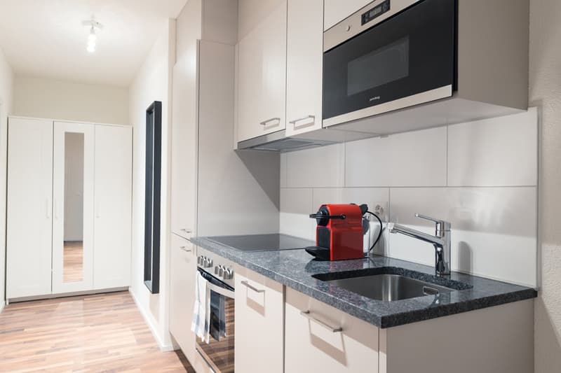 Modern kitchen with white cabinets, black appliances including a microwave and dishwasher, granite countertops, and a red coffee machine on the counter