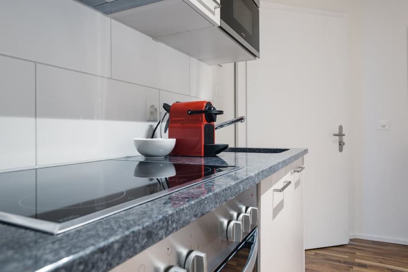 Modern kitchen with granite countertop, built-in stove, and a red coffee machine on the counter