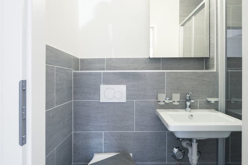 Modern bathroom with gray tile walls, white sink, and shower enclosure