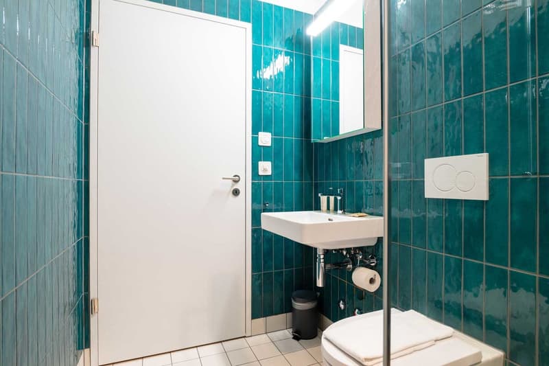 Bathroom with teal tile walls, white door, white sink, and toilet