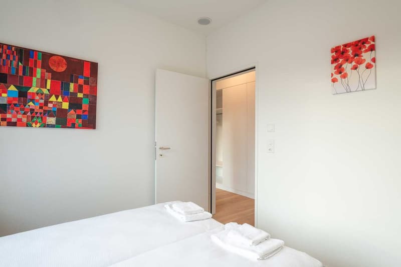 White walls, hardwood floor, large abstract painting, red floral artwork, white bedding, closet door visible
