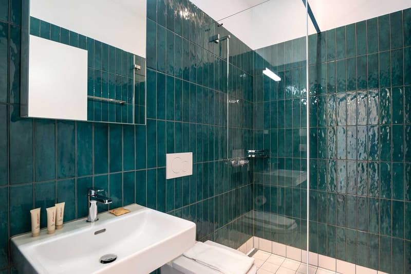 Bathroom with tiled walls in a deep green color, a white sink, and a glass shower enclosure.