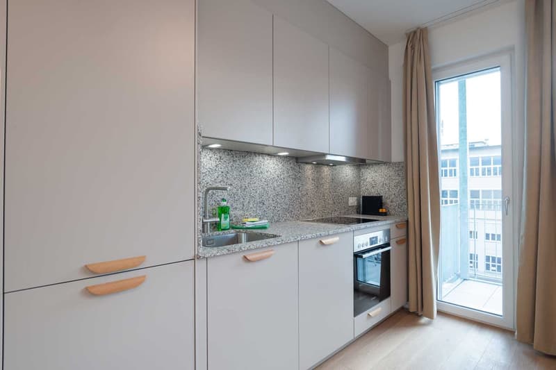 Modern kitchen with white cabinets, granite countertops, built-in oven and dishwasher, large window providing natural light