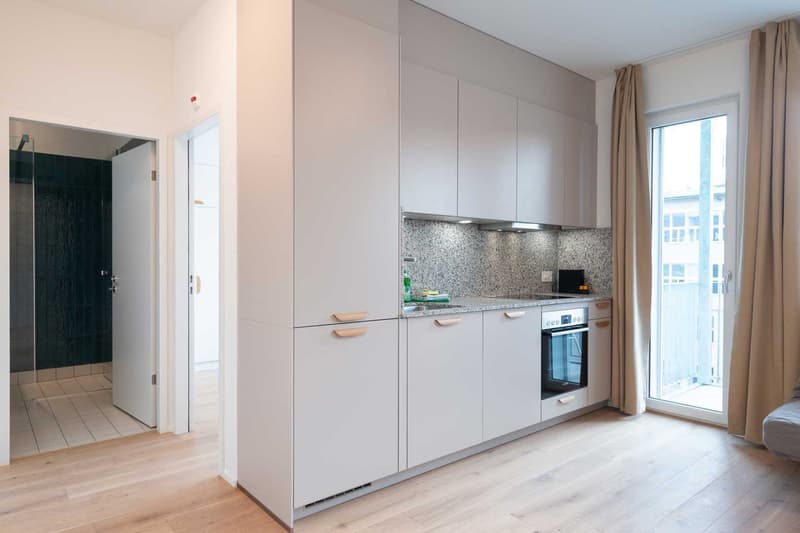 Modern kitchen with white cabinets, granite countertop, built-in oven and dishwasher, large window providing natural light