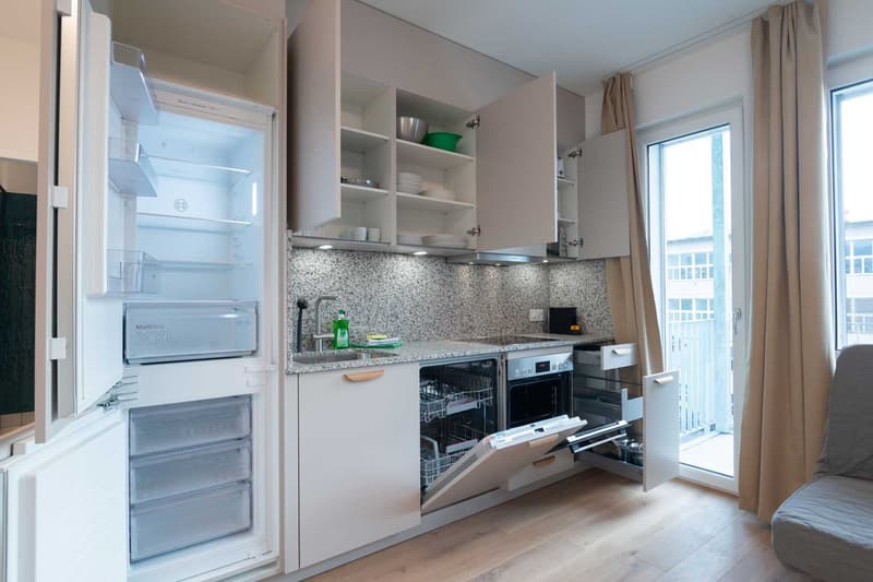 Compact kitchen with built-in appliances, including a refrigerator and dishwasher, granite countertops, and open shelving for storage.
