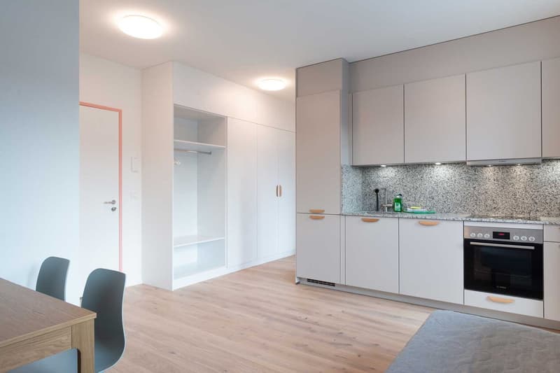 Modern kitchen with gray cabinets, granite countertop, built-in oven, and hardwood flooring. Open layout with dining area and closet space.