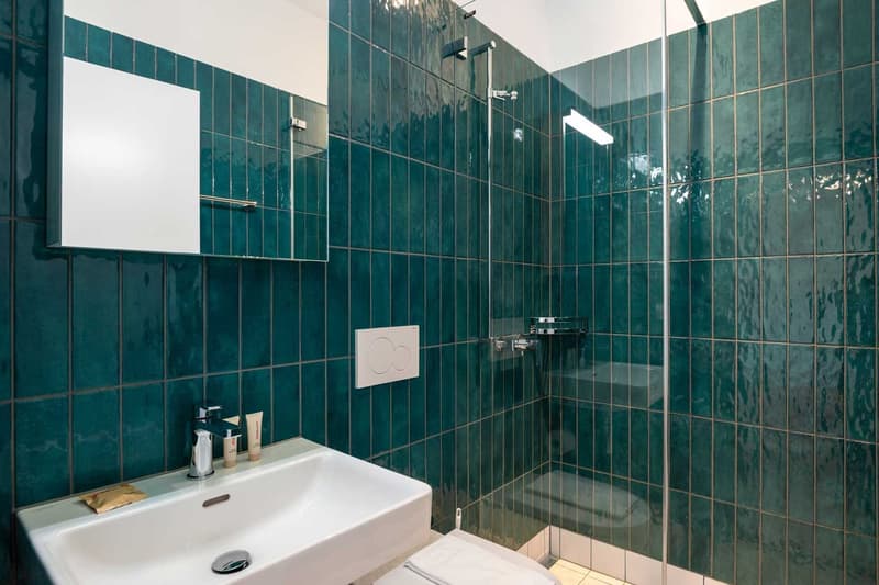 Bathroom with green tiled walls, a white sink, and a glass shower enclosure.