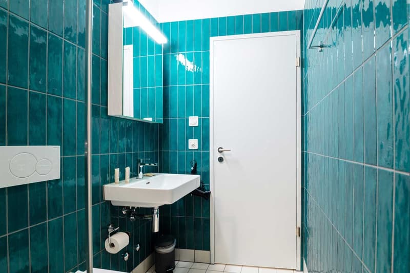 Tiled bathroom with teal green tiles, a white sink, and a white door.