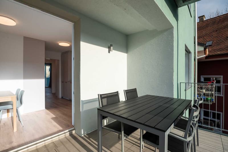 Open-plan living area with dining table and chairs, hardwood flooring, sliding glass door leading to a balcony or terrace