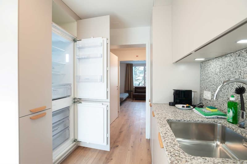 Open kitchen with granite countertops, stainless steel appliances including a refrigerator and dishwasher, hardwood floors, and a view into the adjacent room
