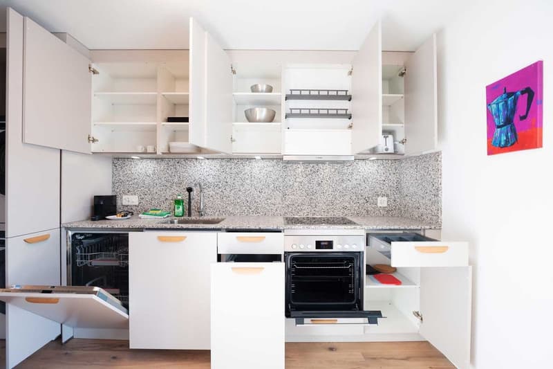 Modern kitchen with white cabinets, granite countertops, built-in oven, dishwasher, and open shelving for storage