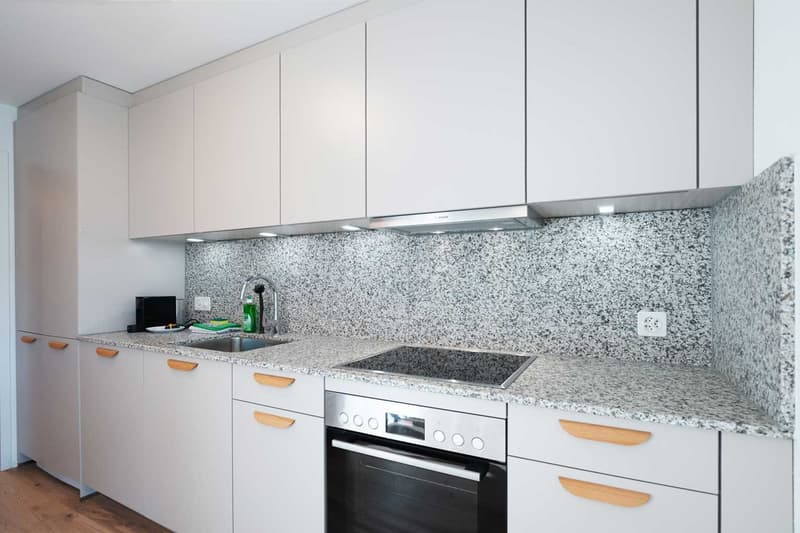 Modern kitchen with white cabinets, granite countertops, built-in oven, and dishwasher