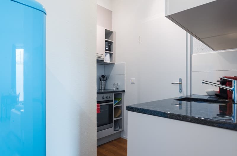 Modern kitchen with white walls, built-in appliances, black granite countertop, and a blue refrigerator
