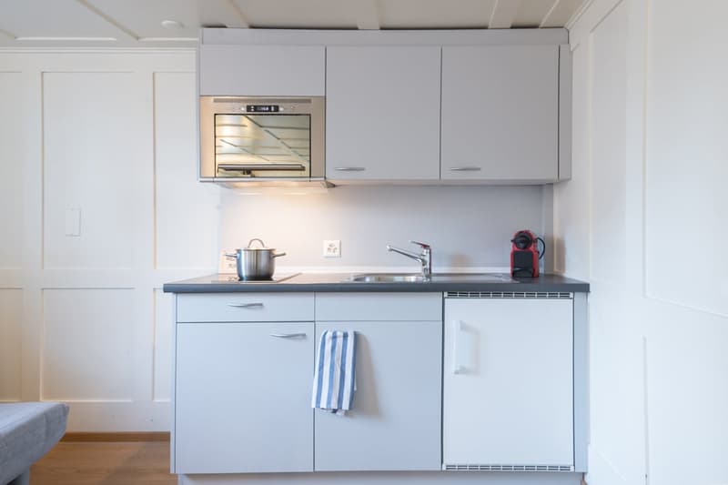 Compact kitchen with white cabinets, built-in oven, sink, and dishwasher
