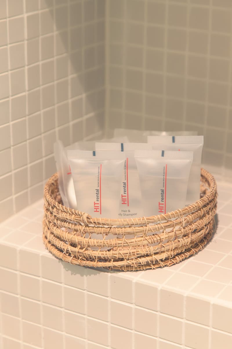 Wicker basket containing hair and body shampoo bottles, placed on tiled bathroom wall