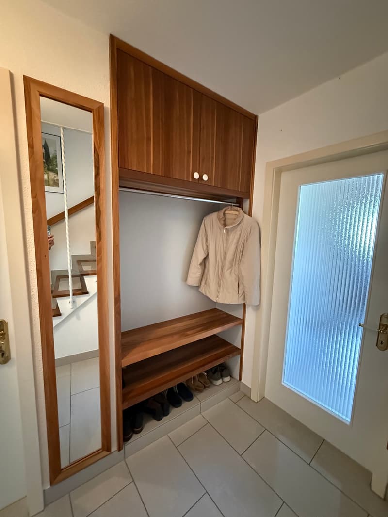 Entrance hall with wooden closet, wooden shelf, mirror, tiles, a pair of shoes, a jacket