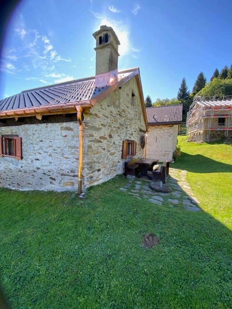 Stone house with copper roof and chimney, wooden seating, grassy yard