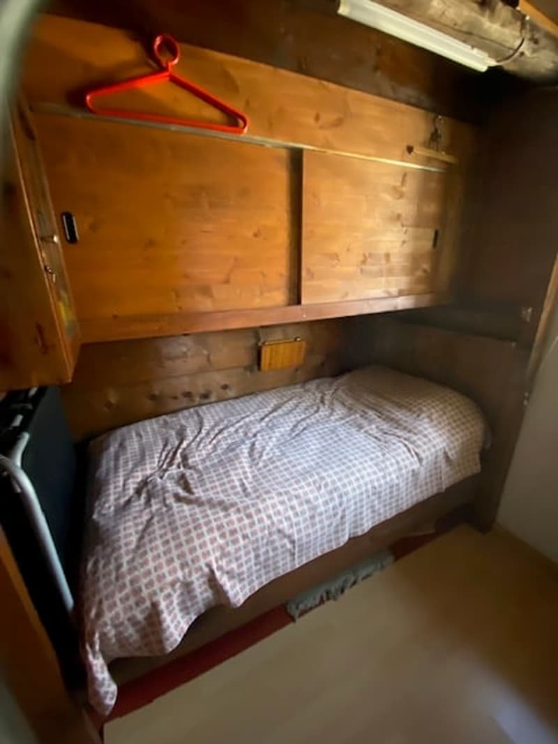 a small bedroom with wooden cabinets above a single bed and wooden walls