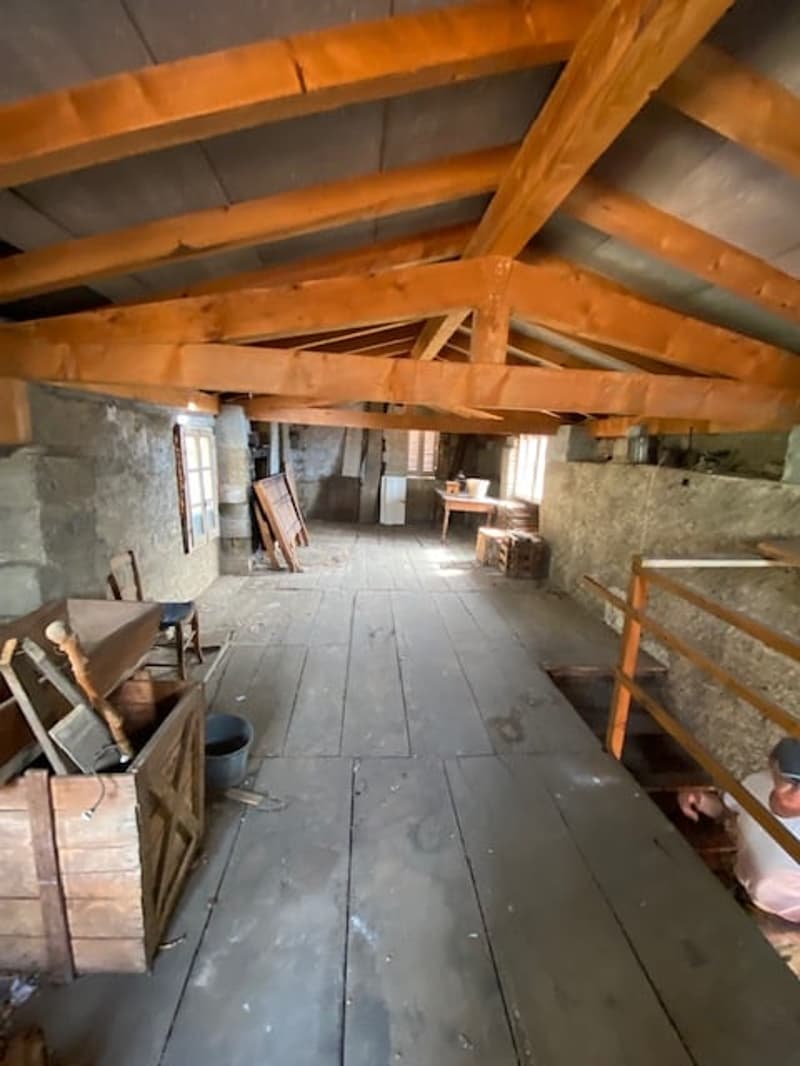unfinished basement with wooden beams and stone walls, several wooden storage boxes and chairs