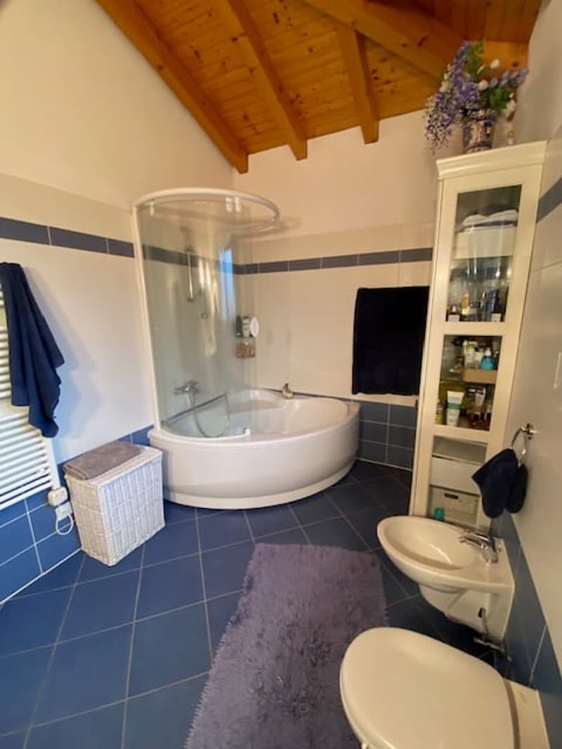 White bathtub, shower enclosure, two sinks, purple rug, blue tiles, white toilet, blue towels, wooden ceiling