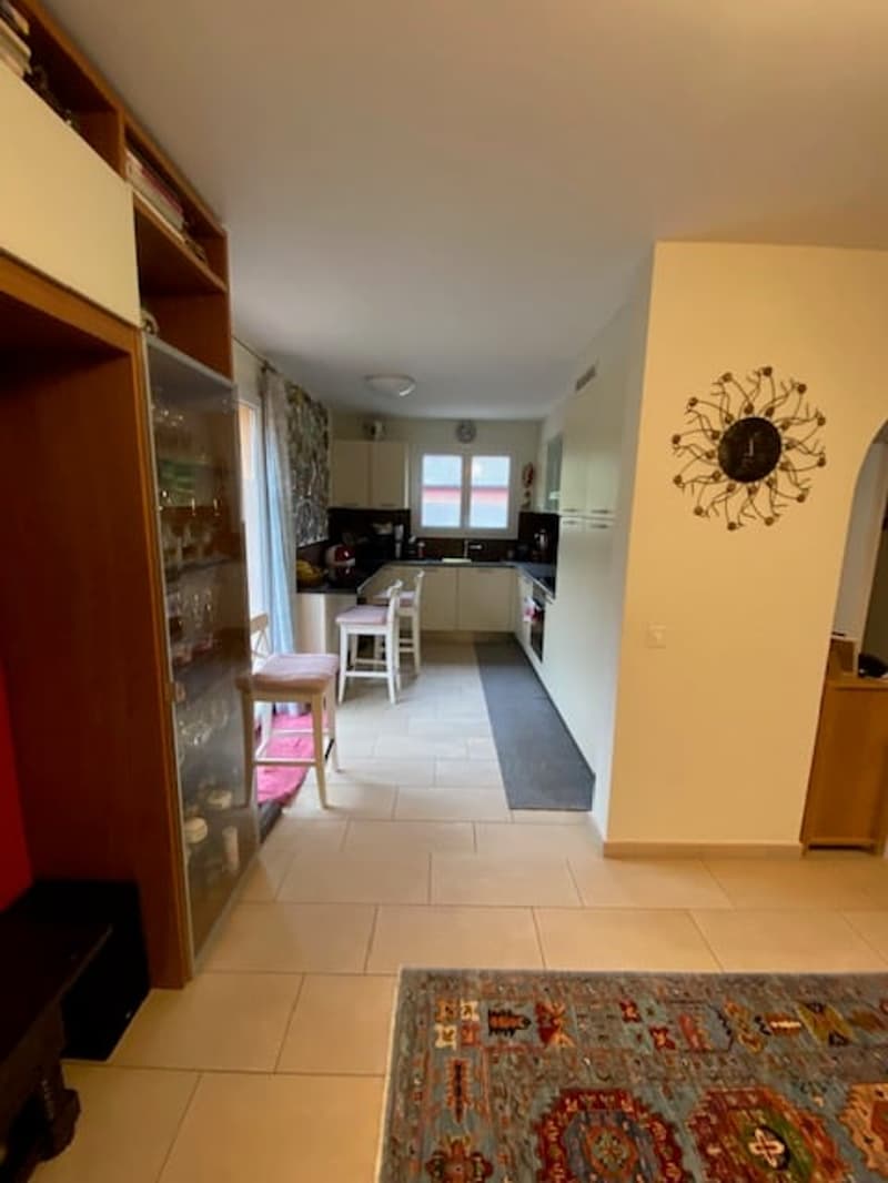 modern interior, tile floor, white walls, two chairs and a stool, wooden cabinet with glass doors, rug, white kitchen, countertop, clock on the wall, window
