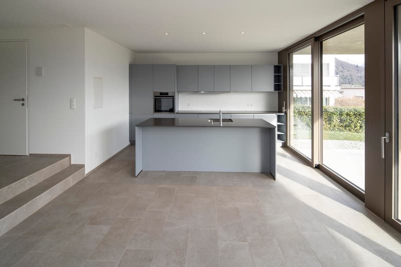 modern open kitchen with island, neutral color scheme, large windows, stainless steel sink, no appliances