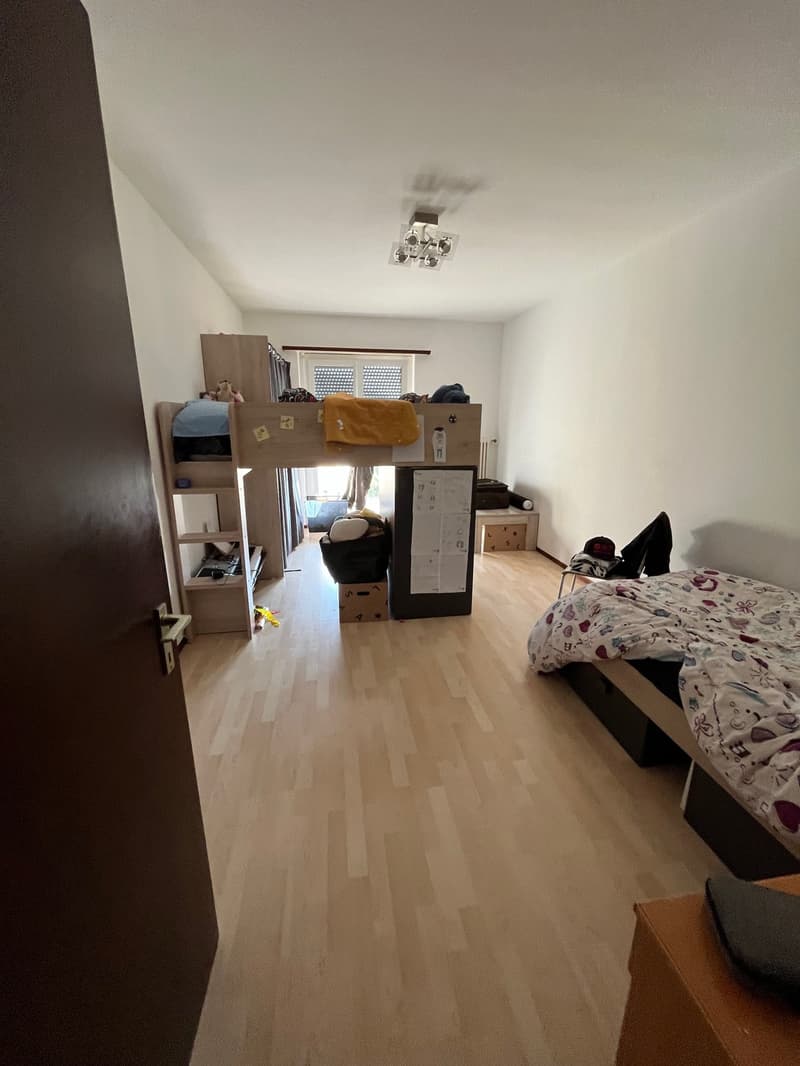 empty room with hardwood floor, two bunk beds, desk, trash can, storage boxes, open door, window with blinds