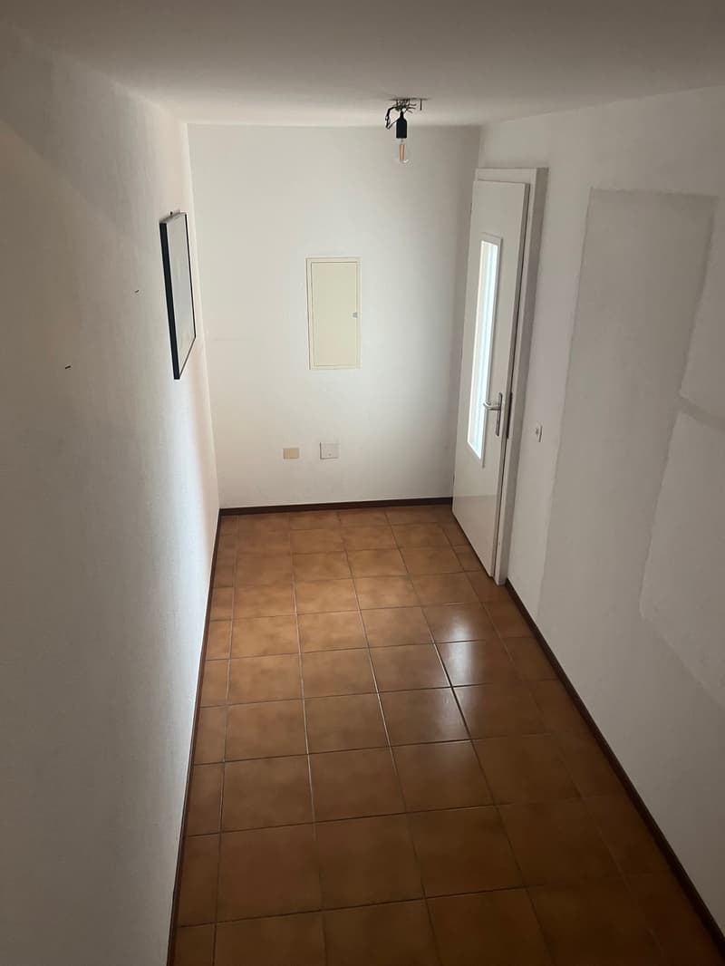 empty hallway with tiled floor, white walls, single light bulb on ceiling, a door