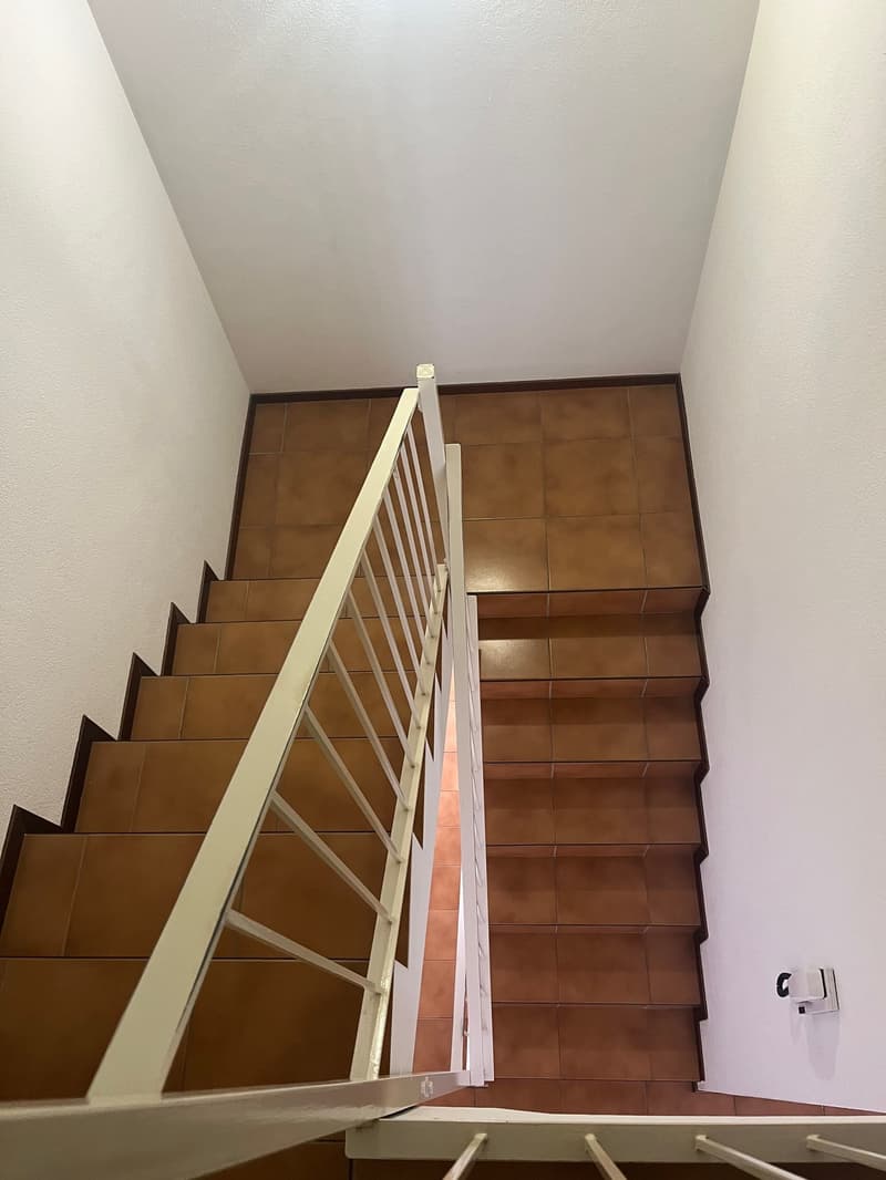White handrail, tiled staircase, tiled risers and steps, tiled landing, wall-mounted switch