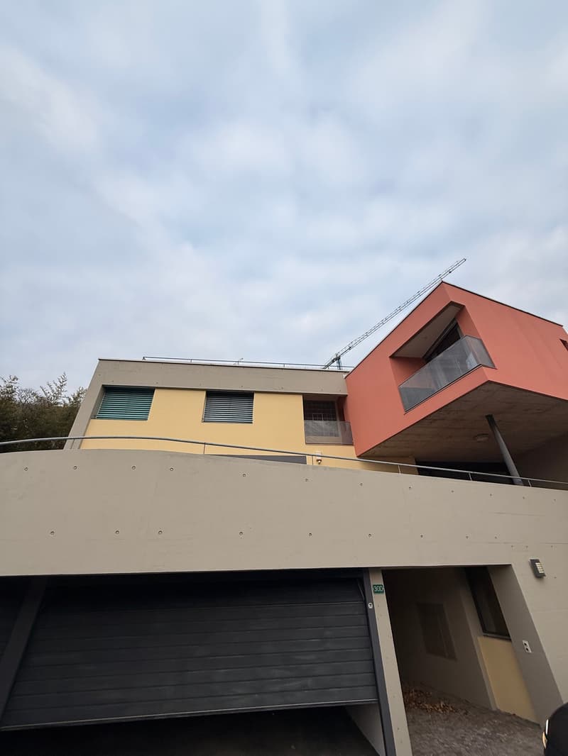 Modern two-story building with yellow and red sections, balconies, garage entrance