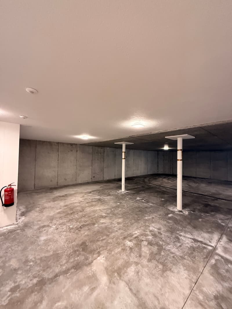Empty concrete garage with pillars, white ceiling and walls, with fire extinguisher, concrete floor