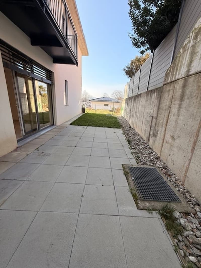 Facade of a building with balcony, sliding glass door, concrete walkway, stone border, and wall.